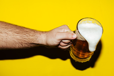 Hand hold mug of beer on yellow backgroundの写真素材