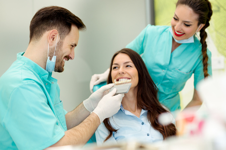 Dentist checking and selecting color of young woman's teethの写真素材