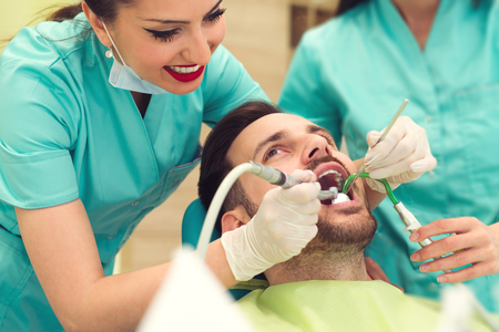 Female dentist examining and working on young male patient. Dentist's office.の写真素材