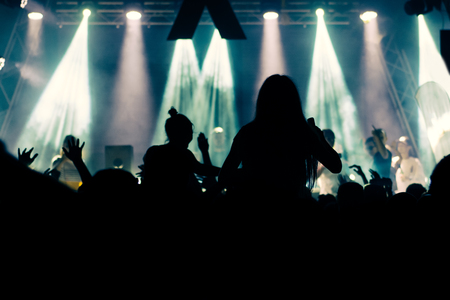 Silhouettes of concert crowd in front of bright stage lightsの写真素材