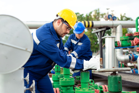 Two petrochemical workers inspecting pressure valves on a fuel tankの写真素材