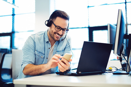 Handsome man in headphones is listening to music using a smartphone