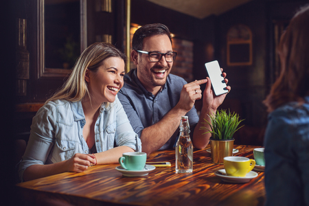 Young couple showing something to friend on the smartphone.の写真素材