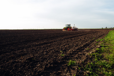 Farmer sowing crops at field with tractor.の写真素材