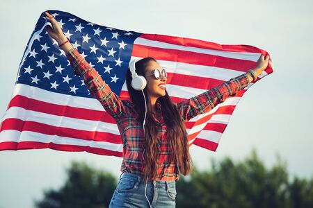 Young girl wearing sunglasses and holding American flag, enjoying music