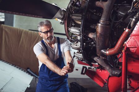 Aircraft mechanic repairs an aircraft engine in an airport hangarの写真素材