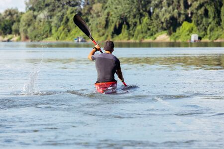 Man athlete paddles a red kayak in summer on river