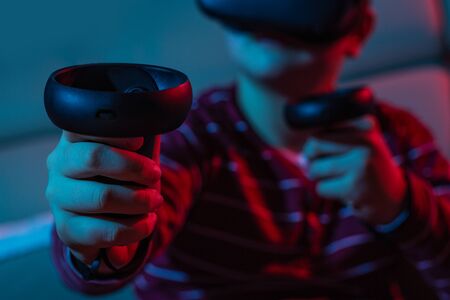 Teenager boy using a Virtual reality headset with goggles and hands motion controllers in playing...