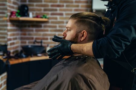 Handsome bearded man is getting beard hairstyle by hairdresser at the barbershop.の写真素材