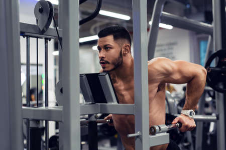 Muscular man working out in gym doing exercises at triceps