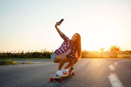 Beautiful young girl sits on longboard in sunny weather.