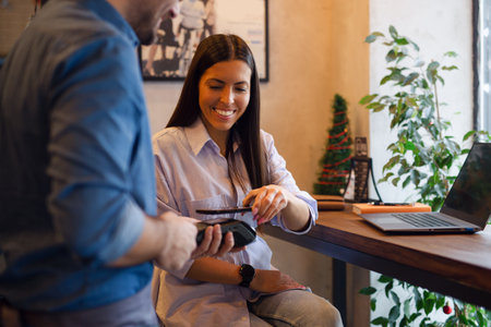 Happy young woman making payment through mobile phone in cafe