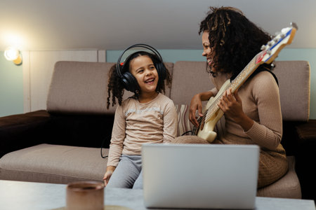 Mom with her daughter playing electric guitar together at home, happy familyの写真素材