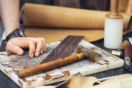 Close up of a shoemaker or artisan worker hands. Leather craft tools on old wood table.