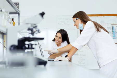 Two female scientists working on a laptop in a laboratory. Focus on the woman