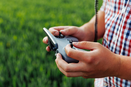 Light skin adult man holds drone controller with both hands while standing in a green field wearing a plaid shirtの写真素材