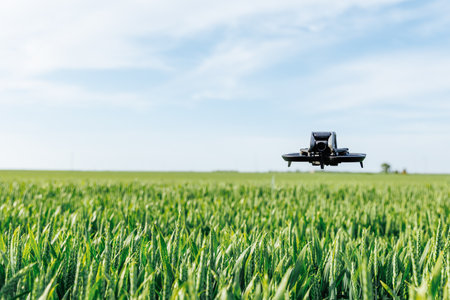 Black drone flying low above green crops with bright sky and distant horizon in a rural agricultural fieldの写真素材