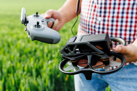 Farmer holding a drone and its remote control standing in a green field, ready to flyの写真素材