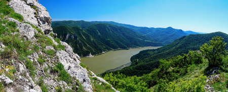 Breathtaking panorama of the danube river meandering through vibrant green hills, viewed from a rocky cliff on a sunny dayの写真素材