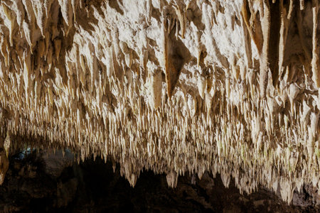 Numerous stalactites hang from the ceiling of a dark cave, showcasing the beauty of nature's formationsの写真素材