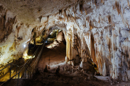 Footpath winding through an ancient cave, illuminated by artificial light, showcasing breathtaking stalactite and stalagmite formationsの写真素材