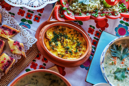 Overhead view of a colorful, floral tablecloth laden with various dishes, including a casserole, soups, salad, and dessertの写真素材