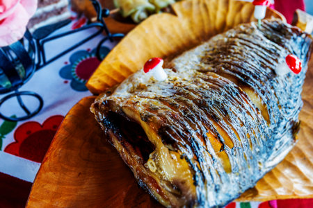 Traditional romanian christmas dish, a grilled fish seasoned and decorated with small plastic mushrooms, served on a wooden plateの写真素材