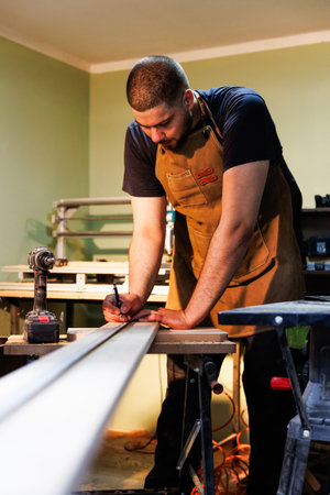 Carpenter meticulously marking measurements on a wooden plank, preparing for precise woodworking in his workshopの写真素材