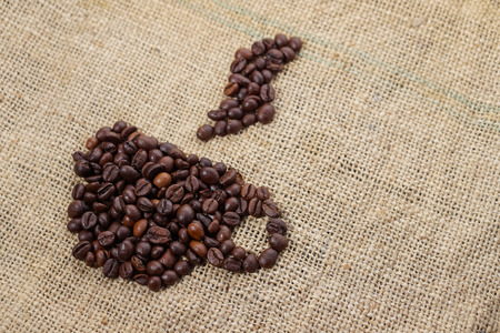 Roasted coffee beans placed in the shape of a cup and placed on sackclotheの写真素材