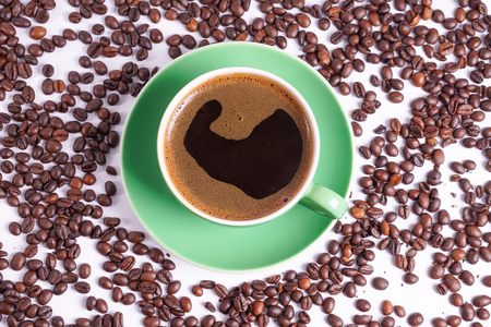 Coffee in green cup surrounded with coffee beansの写真素材