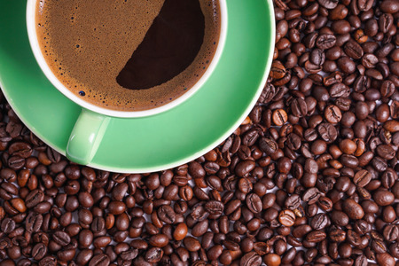Coffee in green cup surrounded with coffee beansの写真素材