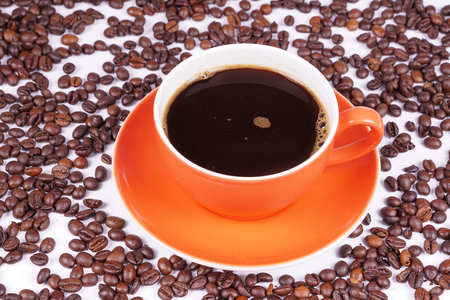 Coffee in orange cup surrounded with coffee beansの写真素材