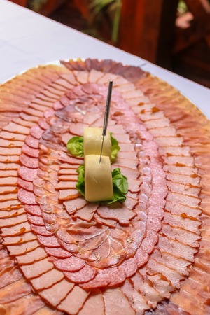 Delicious slices of pork dried meat decorated in circles on large plate. Large plate with meat slices on a wedding.の写真素材