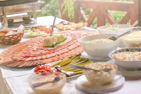 Delicious slices of pork dried meat decorated in circles on large plate surrounded with lot of different salads. Wedding day food table.の写真素材