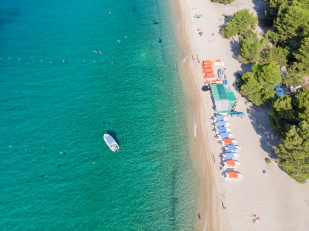 Drone aerial view of sea shore, sandy beach and blue water. Boat near beach with lot of sunshades.の写真素材