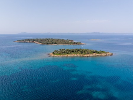 Two small islands surrounded with blue sea water with mountains in background. Drone aerial view.の写真素材