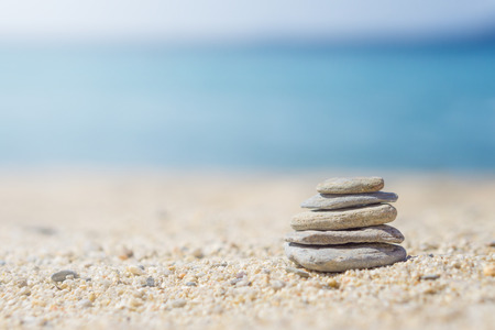 Vertical ordered stones on sand at the beach. Blurred blue sea at background.の写真素材