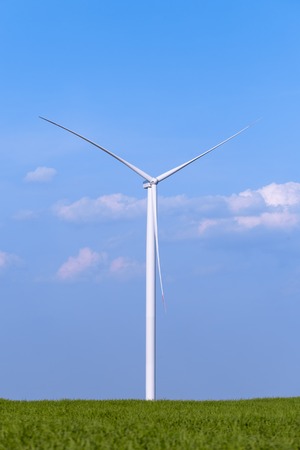 One single windmill turbine on green agricultural field with blue sky in background. Renewable energy wind turbineの写真素材