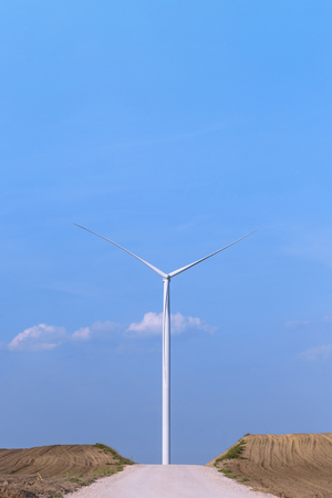 One single windmill turbine in front of road with blue sky in background. Renewable energy wind turbineの写真素材