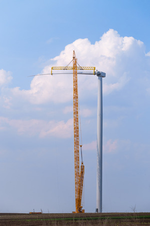 yellow crane tower placing windmill blade with background of blue sky. Wind Turbine Construction.の写真素材