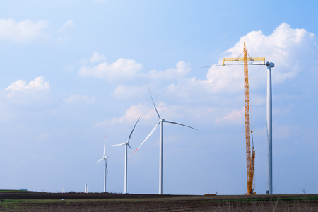 yellow crane tower placing windmill blade with background of blue sky. Wind Turbine Construction.の写真素材