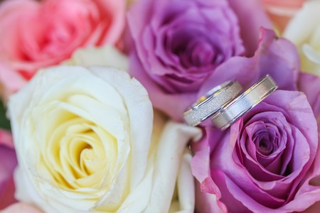 White gold wedding rings on bouquet of purple and white roses.の写真素材