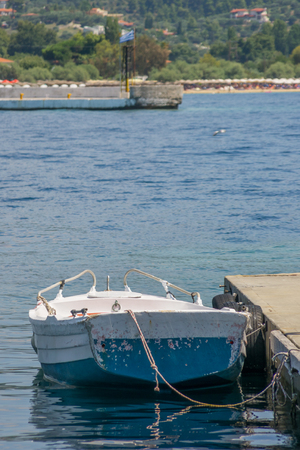 Old small white blue boat anchored next to the dock.の写真素材