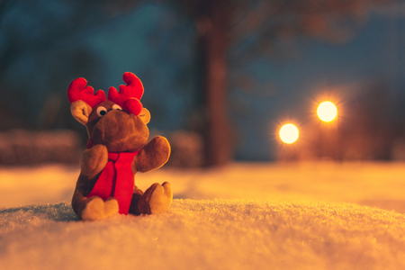 Soft toy reindeer with red scarf sitting on snow outdoor.の写真素材