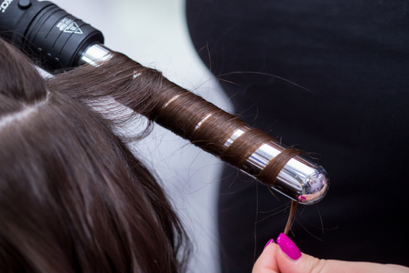 The hairdresser curl hair with figaro in the salon.の販売画像