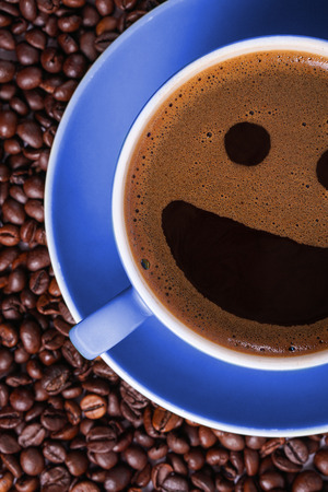 Coffee in blue cup on a table surrounded by coffee beans. Coffee in the shape of a smileの写真素材