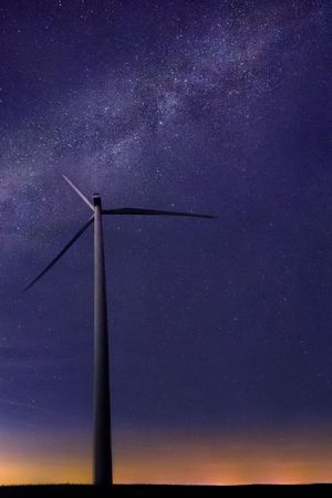 One wind turbine with beautiful milky way in background with bright stars over flat land at midnight