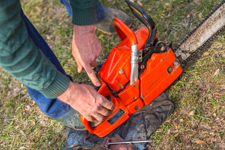 Old man in blue pants starting orange chainsaw.の写真素材