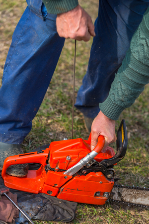Old man in blue pants starting orange chainsaw.の写真素材
