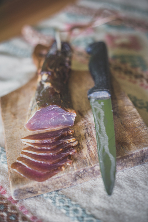 A dried ham on a wooden board cut into snacks with a knife next to it.の写真素材